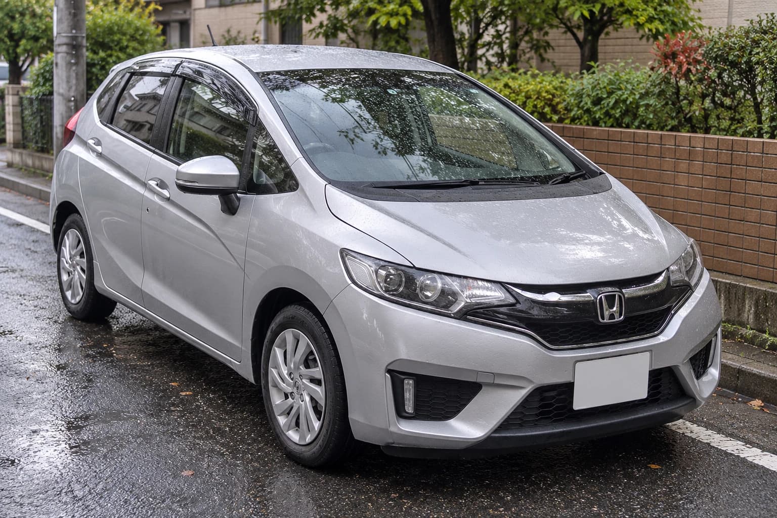 Серебристый Honda Fit третьего поколения GK на мокрой городской улице