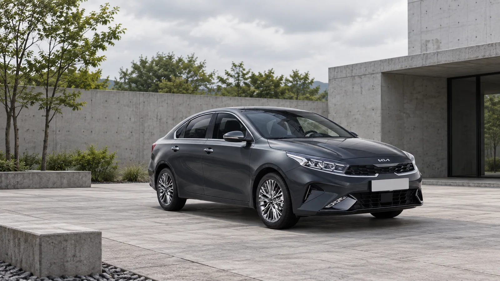 Серый корейский Kia K3 BD после рестайлинга, вид спереди сбоку на фоне светлого бетонного здания